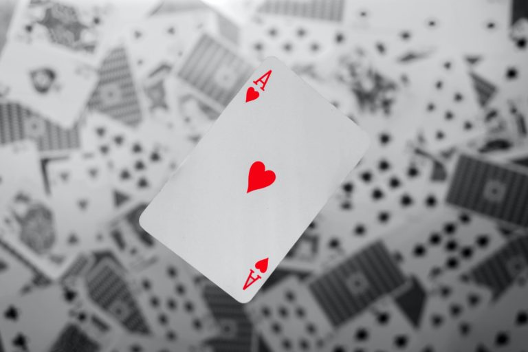Close up of a playing card with the ace of hearts floating above the rest of the cards scattered below.