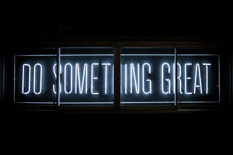Close up of a white neon sign saying do something great on a black wall.