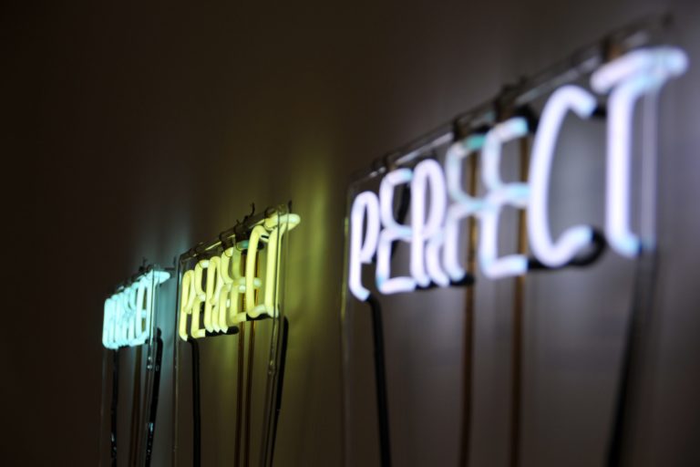 Close-up of three neon signs saying perfect. Signs are blue, yellow and purple.