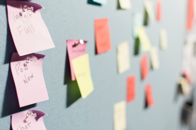 Close up of colorful sticky notes pinned to a board. Three are clear in the foreground and the rest are out of focus in the background.
