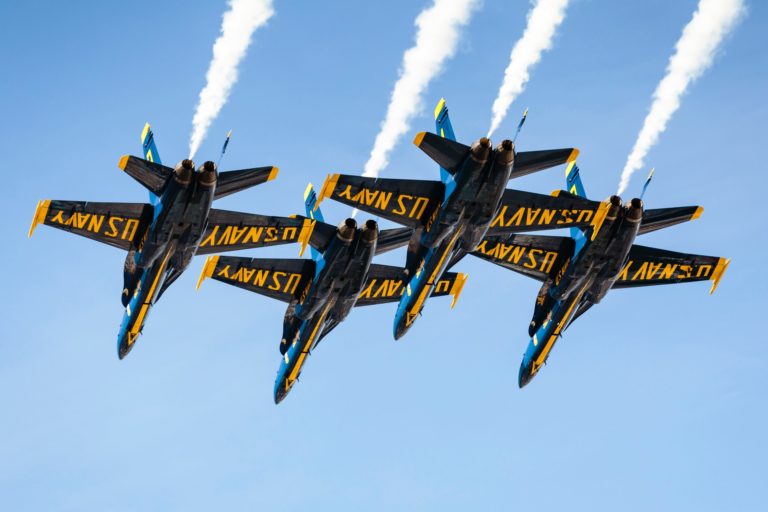 Four U.S. Navy Jets are flying in formation against a blue sky.